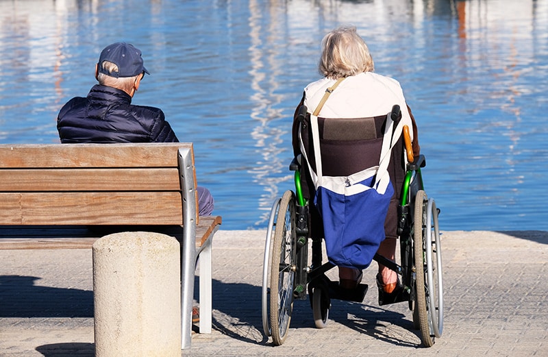Senior Couple Sitting at Waters Edge in Wheelchair